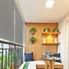 A cozy balcony setup with a roller blind, seating, a small table, and decorative plants. Náhled obrázku produktu