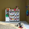 A white toy storage unit filled with toys, placed on a patterned rug in a room with brown walls. Produktbild-Vorschau