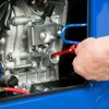 A close-up view of a person's hand using a red tool to interact with a generator's engine. Produktbild-Vorschau