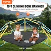 Two young children are sitting on a black hammock attached to a colorful climbing dome structure in an outdoor setting with a lake and trees in the background. Produktbild-Vorschau