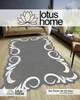 A rug with a decorative border is placed on a wooden floor in a living room setting, with a sofa and window in the background. Produktbild-Vorschau