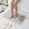 A person's legs are shown standing on a beige bath mat in a bathroom, next to a bathtub. White slippers are on the floor in front of the mat. Produktbild-Vorschau