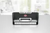 A vacuum sealer is placed on a table in front of a blurred kitchen background. Podgląd zdjęcia produktu