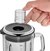 A hand is holding a measuring cup over the lid of a blender. Voir les images du produit