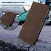 A brown leather phone case is shown in a close-up, angled view against a textured, cracked ground background. In the background, a green industrial machine is visible. Produktbild-Vorschau