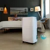 A woman is sitting on a bed in a bedroom, and a white dehumidifier is in the foreground. Produktbild-Vorschau