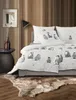 A bedroom scene with a bed dressed in penguin-themed bedding, a side table with vases, and a floor lamp. Produktbild-Vorschau