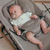 A baby is lying in a gray baby bouncer with a pacifier in its mouth. Podgląd zdjęcia produktu