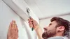 A man is using a tool to attach something to a wall. Produktbild-Vorschau