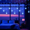 A bedroom with a large window overlooking a city at dusk, decorated with blue snowflake string lights. Náhled obrázku produktu
