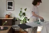 A woman is ironing clothes on an ironing board in a well-lit room. Produktbild-Vorschau