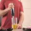 A person is using an immersion blender to blend food in a glass container. Produktbild-Vorschau