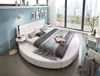 A modern bedroom with a large round bed, floor lamp, and a city view from the window. Produktbild-Vorschau