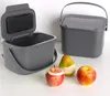 Two gray compost bins are shown on a white surface, with three pieces of fruit in the foreground. Anteprima dell’immagine prodotto