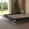 A bed frame with wooden slats is shown in a bedroom setting, with a window and curtains in the background. Náhled obrázku produktu