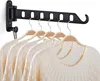 A black wall-mounted retractable clothes drying rack with several white sweaters hanging on wooden hangers. Produktbild-Vorschau