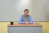 A man sits behind a desk in front of a whiteboard. Produktbild-Vorschau