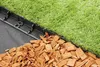 A close-up view of a garden border installation, showing artificial grass, a black plastic border, and wood chips. Produktbild-Vorschau