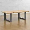 A wooden coffee table with gray metal legs is shown in a room with a white brick wall and wooden floor. Náhled obrázku produktu