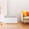 A white Xiaomi electric heater is placed on a wooden floor in a room with a couch and pillows in the background. Produktbild-Vorschau