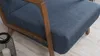 Close-up of a blue fabric armchair with wooden frame on a light wooden floor. Produktbild-Vorschau