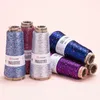 Several spools of glitter yarn with sequins are arranged on a light pink background. Some spools are standing upright, while others are lying down. Produktbild-Vorschau