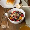 A bowl of cereal with berries and a bun on a wooden table. Produktbild-Vorschau