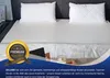 A bed with two white pillows and a white mattress topper, with a golden seal and text overlay. Produktbild-Vorschau