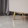 A close-up shot of the gold legs of a white kommode on a marble floor, with a grey curtain in the background. Produktbild-Vorschau