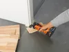 A person is using an oscillating multi-tool to cut a piece of wood flooring near a doorway. Náhľad obrázku produktu