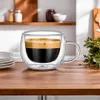 A double-walled glass mug filled with dark coffee and a layer of crema sits on a wooden table. Náhled obrázku produktu