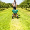 A person is using a spreader in a grassy orchard. Produktbild-Vorschau