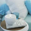 A white diffuser is placed on a book next to a glass of water on a side table, with pillows in the background. Voir les images du produit