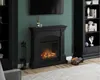 A black electric fireplace with a realistic flame effect is shown in a living room setting, with a bookshelf and a TV in the background. Produktbild-Vorschau