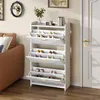 A white shoe cabinet with multiple flip-down doors is shown in a room next to a brown sofa and a white door. Podgląd zdjęcia produktu