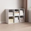 A white cube bookshelf filled with various items, placed against a white wall and next to a curtain. Produktbild-Vorschau