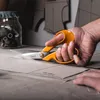 A person's hand is holding orange-handled scissors and cutting a pattern on a piece of paper. Podgląd zdjęcia produktu