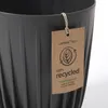 A close-up of a dark gray plant pot with a tag attached. Voir les images du produit