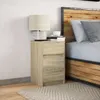 A bedside table with a lamp and books next to a bed. Anteprima dell’immagine prodotto