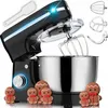 A black stand mixer with a silver bowl is shown with several gingerbread cookies in front of it. The mixer has its head tilted up, revealing the whisk attachment. Several other attachments are shown in the upper right corner, and a white spatula is in the  Produktbild-Vorschau