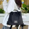Schwarzer Nylonrucksack mit weißem ineinandergreifendem Logo, getragen von einer Person in einem weißen Hoodie Produktbild-Vorschau