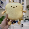 A hand holding a plush toy shaped like a slice of toast, with a smiling face, in a domestic setting. Náhľad obrázku produktu
