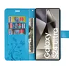 A blue flip wallet case for a Samsung Galaxy S24 Ultra, shown open with cards and cash inserted, and the phone screen displaying a geometric pattern. Produktbild-Vorschau