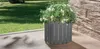 A gray planter with white flowers sits on a tiled patio next to a stone wall, with a lawn in the background. Produktbild-Vorschau