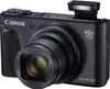 A black Canon PowerShot SX740 HS digital camera is shown from the front-left angle against a white background. The camera has its pop-up flash extended. Podgląd zdjęcia produktu