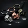 Three angel-shaped keychains in different metallic finishes are displayed against a dark background. Produktbild-Vorschau
