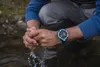 A person is washing their hands in a stream, wearing a smartwatch. Voir les images du produit