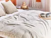 A cozy bedroom scene with a beige throw blanket draped over a bed. Podgląd zdjęcia produktu