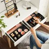 A person's hands are shown organizing makeup and jewelry on a white vanity table with drawers. Produktbild-Vorschau