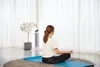 A woman meditating on a yoga mat in a bright room with sheer curtains. Voir les images du produit